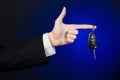 Business and gift theme: car salesman in a black suit holds the keys to a new car on a dark blue background in studio Royalty Free Stock Photo