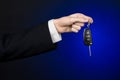 Business and gift theme: car salesman in a black suit holds the keys to a new car on a dark blue background in studio Royalty Free Stock Photo