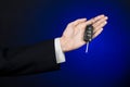 Business and gift theme: car salesman in a black suit holds the keys to a new car on a dark blue background in studio Royalty Free Stock Photo