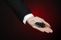 Business and gift theme: car salesman in a black suit holds the keys to a new car on a dark red background in studio Royalty Free Stock Photo