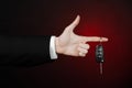 Business and gift theme: car salesman in a black suit holds the keys to a new car on a dark red background in studio Royalty Free Stock Photo