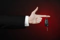 Business and gift theme: car salesman in a black suit holds the keys to a new car on a dark red background in studio Royalty Free Stock Photo