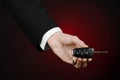 Business and gift theme: car salesman in a black suit holds the keys to a new car on a dark red background in studio Royalty Free Stock Photo