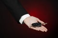 Business and gift theme: car salesman in a black suit holds the keys to a new car on a dark red background in studio Royalty Free Stock Photo