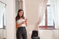 A business girl with a phone in her hand, smiling, stands in a bright room