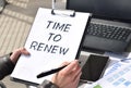 Business girl works at the table outdoors. The girl is holding a tablet for papers with the inscription TIME TO RENEW. Conceptual