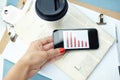 Business on the go. Hand holding smartphone with bar chart on screen with disposable cup, pen, binder clip, newspaper Royalty Free Stock Photo