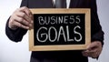 Business goals written on blackboard, businessman holding sign, strategy Royalty Free Stock Photo