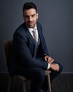 On that business grind. Studio shot of a stylish young businessman sitting on a chair against a gray background. Royalty Free Stock Photo