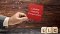 Business hand holding a note with LLC text, the acronym of Limited Liability Company with a row of wooden cubes with LLC text