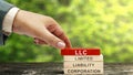 Business hand put a stack of wooden blocks with LLC text, the acronym of Limited Liability Company