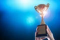 Business hands holding trophy cup on deep blue background. Royalty Free Stock Photo
