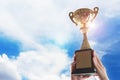 Business hands holding trophy cup on sky background. Royalty Free Stock Photo