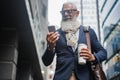 Business hipster senior man using mobile phone while walking to work with buildings in background - Focus face Royalty Free Stock Photo