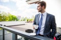 Business, hot drinks and people and concept - young serious businessman with paper coffee cup over office building. Royalty Free Stock Photo