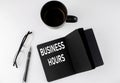 BUSINESS HOURS written text in small black notebook with coffee , pen and glasess on white background. Black-white style Royalty Free Stock Photo