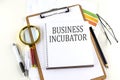 BUSINESS INCUBATOR text on notebook with clipboard on white background