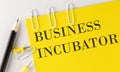 BUSINESS INCUBATOR word on the yellow paper with office tools on white background