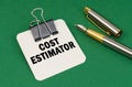 On a green surface, a pen and a sheet of paper with the inscription - Cost estimator