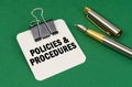 On a green surface, a pen and a sheet of paper with the inscription - Policies and Procedures