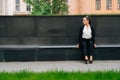 A business lady in a black, stern suit sits on a bench outside work at lunchtime. Customer`s waiting concept