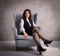 Business lady: a female boss in a gray armchair against a gray wall background. Royalty Free Stock Photo