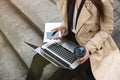 Business lady holding laptop on her knees with coffee and phone in hands working during lunch break on the stairs near office, Royalty Free Stock Photo