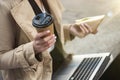 Business lady holding laptop on her knees with cup of coffee and sandwich in her hands sitting near office during lunchbreak , Royalty Free Stock Photo