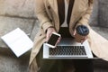 Business lady holding laptop on her knees with cup of coffee and smartphone in hands sitting on the stairs near office during Royalty Free Stock Photo