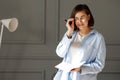 Business lady wearing a white t-shirt, blue shirt and light jeans, is standing on a gray background with a white lamp, holding a Royalty Free Stock Photo