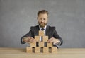 Business leader sitting at office desk and building pyramid out of wooden blocks Royalty Free Stock Photo