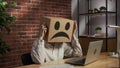 Portrait of a woman in a cardboard box with a negative emoji on her head. Employee sitting at desk, working on laptop Royalty Free Stock Photo