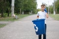 A business-like teenage boy holding a blue recycling bin and speaking on a phone on a blurred natural background. Royalty Free Stock Photo