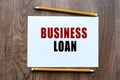 BUSINESS LOAN is written in a notebook which lies on a wooden table. Lettering on a business or financial theme. Business concept