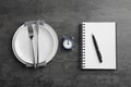 Business lunch concept. Plates, cutlery, alarm clock, notebook and pen on gray textured background, flat lay Royalty Free Stock Photo