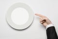 Business lunch and healthy food theme: man's hand in a black suit holding a white empty plate and shows finger gesture on an