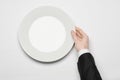 Business lunch and healthy food theme: man's hand in a black suit holding a white empty plate and shows finger gesture on an