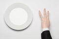 Business lunch and healthy food theme: man's hand in a black suit holding a white empty plate and shows finger gesture on an Royalty Free Stock Photo