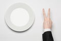 Business lunch and healthy food theme: man's hand in a black suit holding a white empty plate and shows finger gesture on an Royalty Free Stock Photo