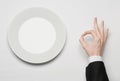 Business lunch and healthy food theme: man's hand in a black suit holding a white empty plate and shows finger gesture on an Royalty Free Stock Photo