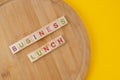 Business lunch menu concept. Scrabble letter tiles on wooden table. Yellow background
