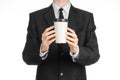 Business lunches coffee theme: businessman in a black suit holding a white blank paper cup of coffee with a brown plastic cap isol Royalty Free Stock Photo