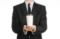 Business lunches coffee theme: businessman in a black suit holding a white blank paper cup of coffee with a brown plastic cap isol Royalty Free Stock Photo