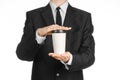 Business lunches coffee theme: businessman in a black suit holding a white blank paper cup of coffee with a brown plastic cap isol Royalty Free Stock Photo