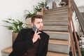 Business man with a beard sitting on the stairs in a cafe, talking on the phone and looking away Royalty Free Stock Photo