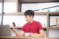 The business man with casual  red t-shirt messaging on mobile phone, drinking coffee and eating sandwich, Young man working on Royalty Free Stock Photo