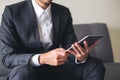 A business man in a gray suit sitting on sofa holding , using and looking at tablet pc for work Royalty Free Stock Photo