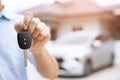 Business man hand holding car keys front with new car on background. parking in front of the house. transportation concept