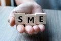 Business man hand holding wooden cube with SME text Small Medium Enterprise on table background. Financial, marketing and