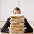 Business man hiding behind tall stack of folders